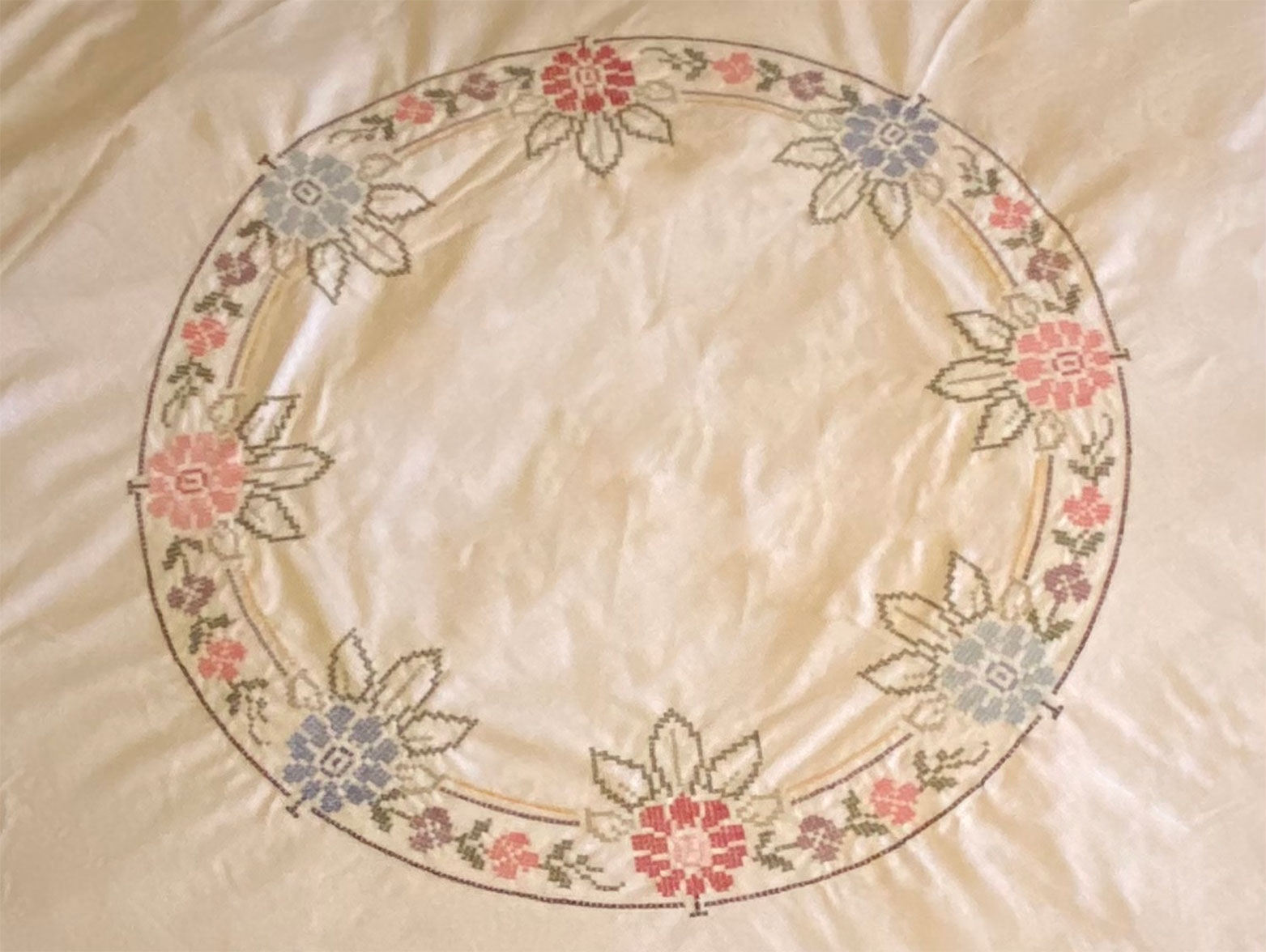 A tablecloth with a large circle. The circle is made from a needlepoint pattern of colourful flowers. The artwork is by Antoinette Charlebois.
